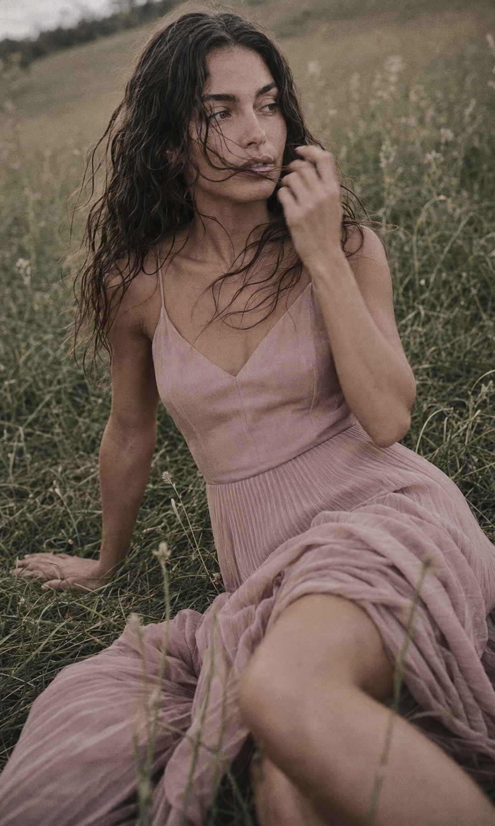 Petite model with a fuller bust seated in a wildflower field, wearing a rose pleated midi dress with a fitted V-neck bodice.