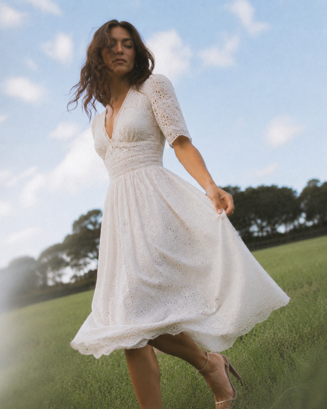 Petite model in an ivory eyelet midi dress moving through a sunlit field.