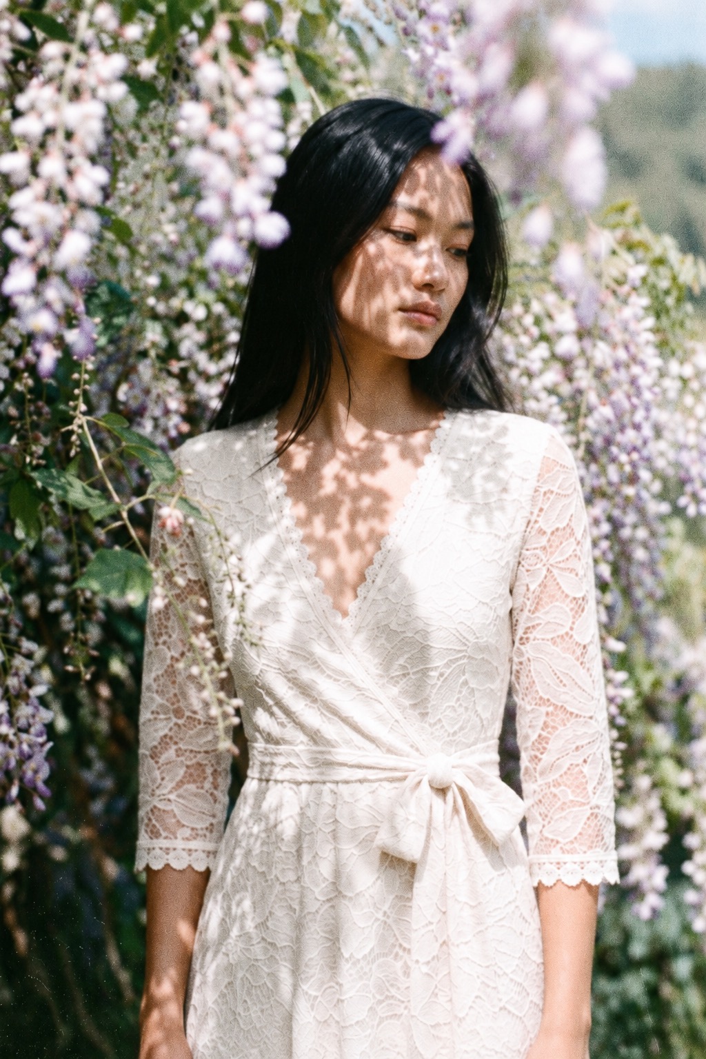 Woman in the ivory Maribel lace wrap dress beneath flowering wisteria