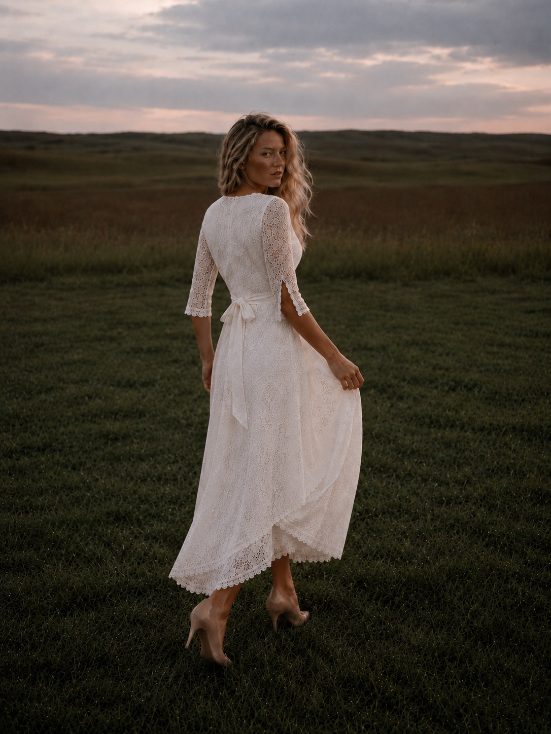 Woman in ivory lace dress walking through grass at sunset