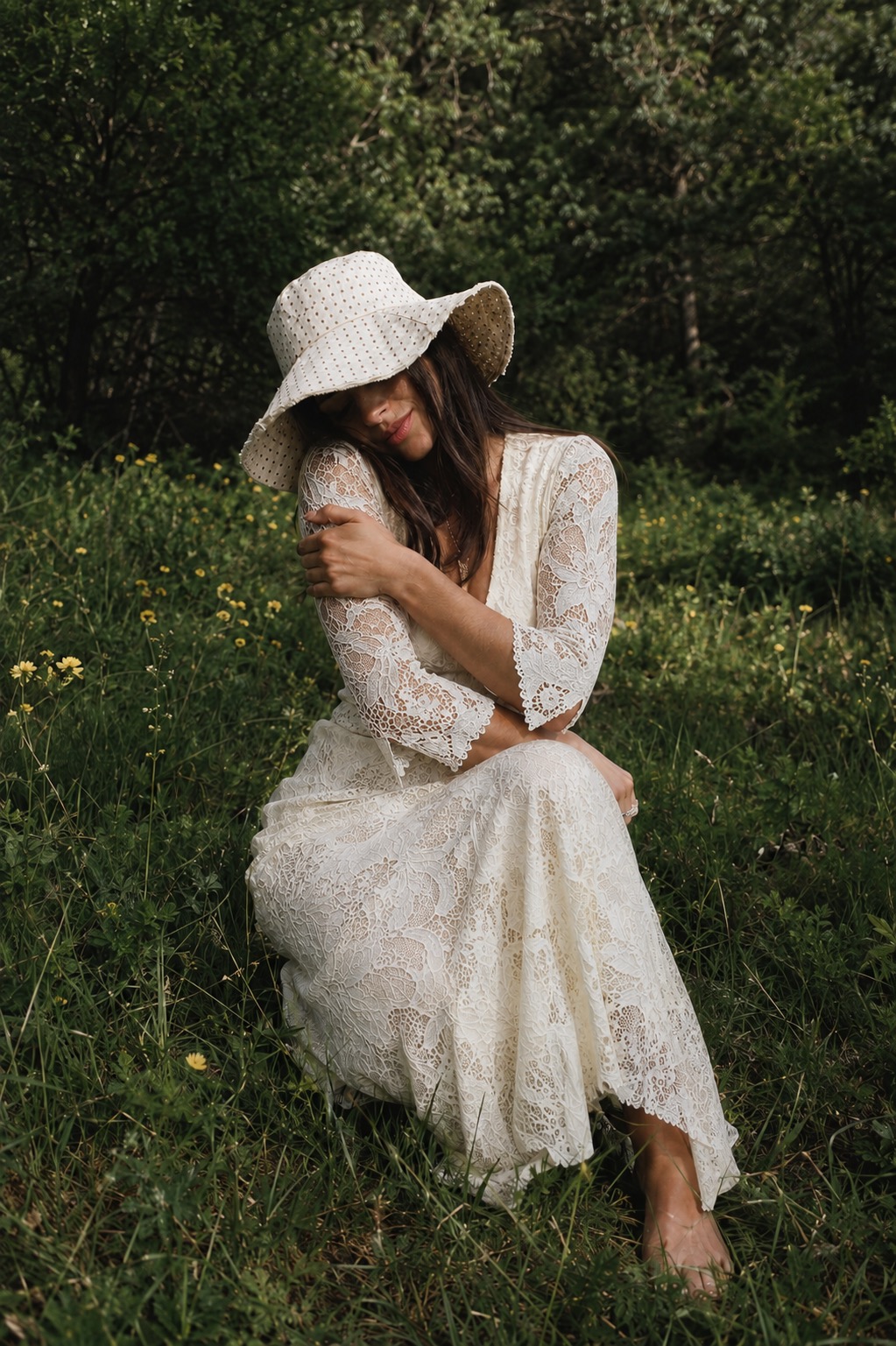 Petite woman seated in a meadow in an eyelet sun hat and scalloped lace dress