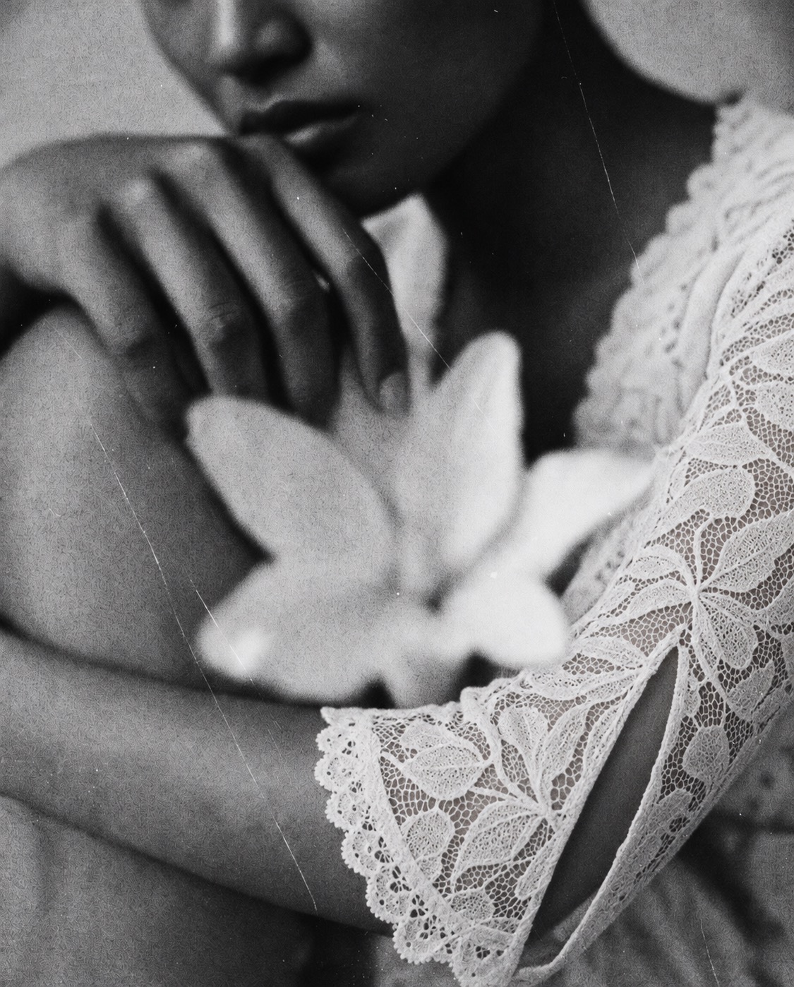 Black and white close-up of a woman in a floral lace sleeve holding a white flower